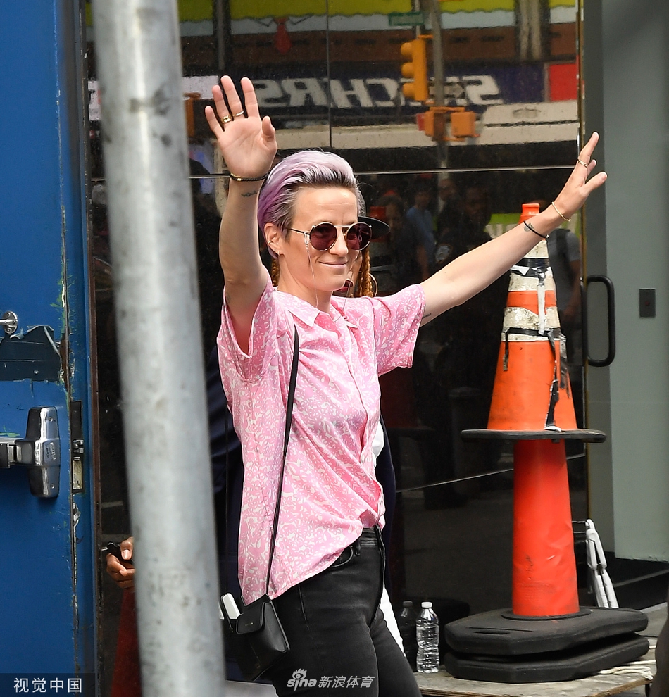 拉皮诺埃将世界杯冠军奖杯高高举过头顶，金色的奖杯在阳光下闪耀。她身后是模糊的欢呼人群和纽约标志性的建筑。她仰头望向奖杯，这一刻的荣耀与喜悦，通过她飞扬的神采和有力的姿态，感染着每一个注视她的人。