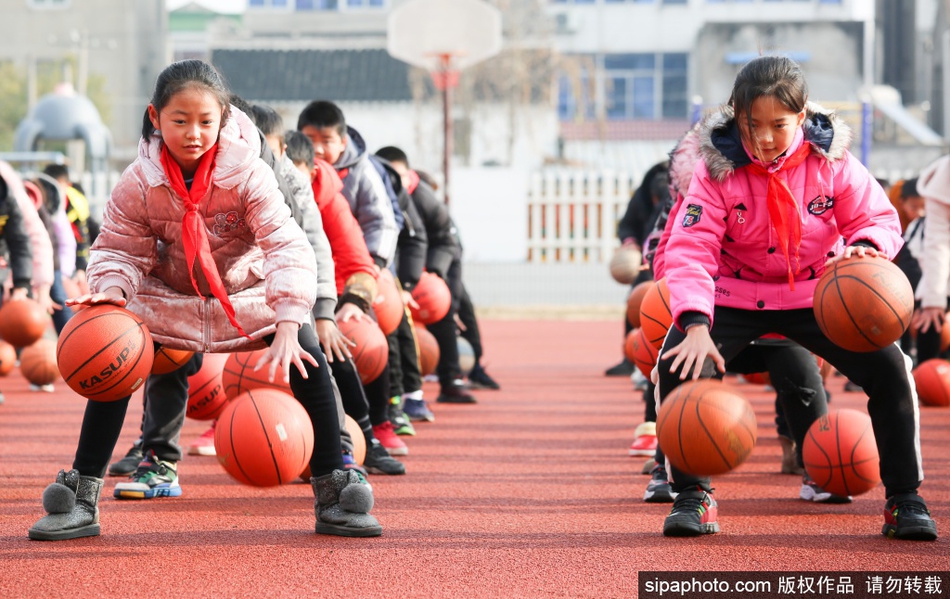 一名高年级学生正在为低年级的“小球友”纠正拍球姿势，大手帮小手，认真的模样仿佛一位小教练，传递着对篮球的共同热爱。