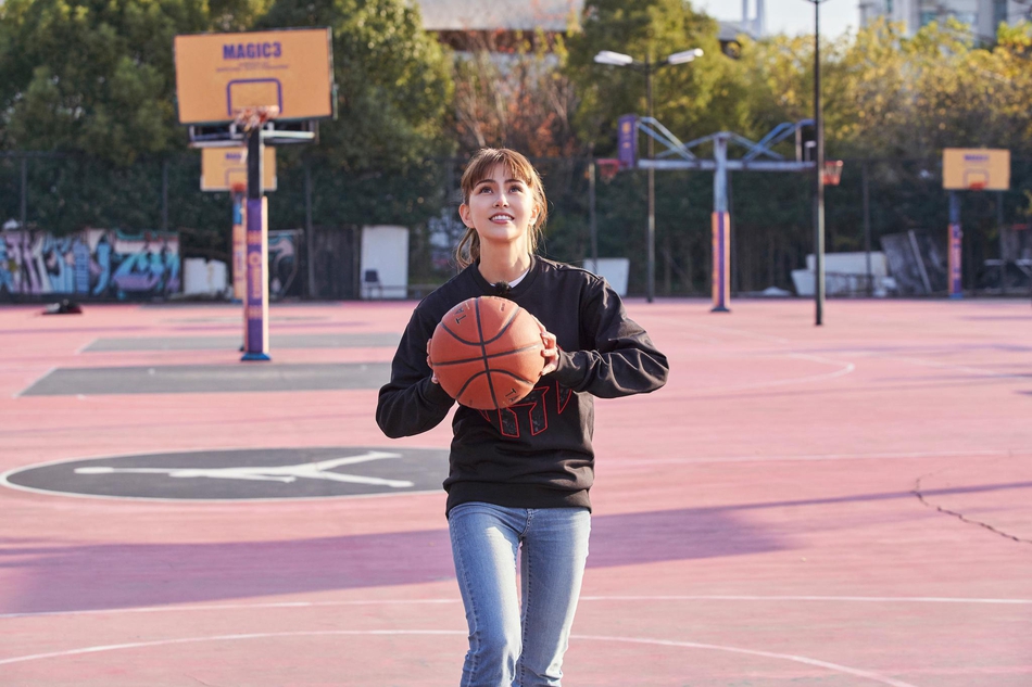 球场上，昆凌成功投篮后，篮球还停留在篮筐边沿，她抬头望向那颗即将落下的球，脸上洋溢着自信而灿烂的笑容。