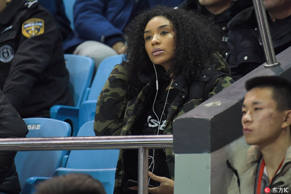 韦弗的妻子全神贯注地凝视着赛场方向，周围球迷的喧嚣仿佛与她隔绝，此刻她的心中只有对爱人最纯粹的支持，那一抹鲜艳的围巾恰如她火热的内心。