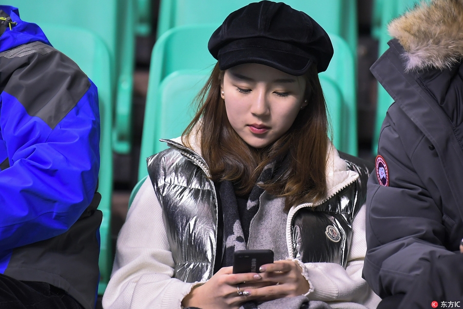 两位闺蜜球迷手持辽宁男篮的助威围巾，脸颊上贴着闪亮的球队贴纸，在喧闹的看台上窃窃私语，分享着对今晚大胜的期待。