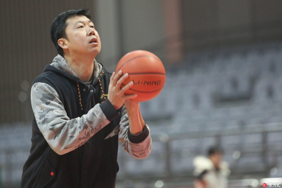 王治郅在训练馆中央背身持球，眼神专注地盯着篮筐，准备向年轻球员演示内线进攻步伐。
