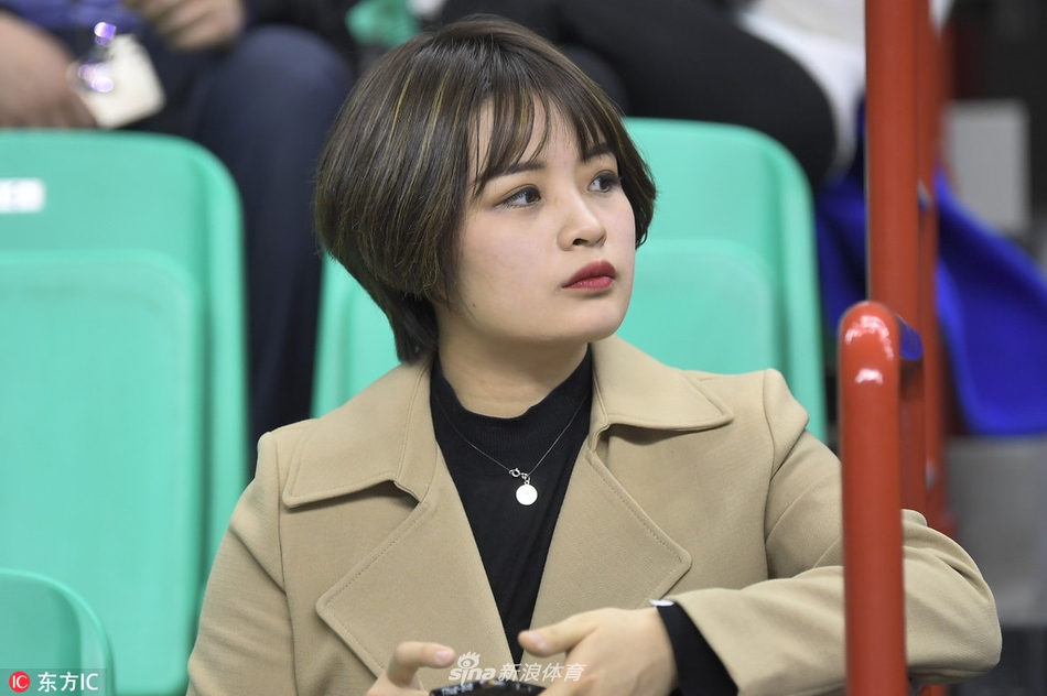 一位穿着白色上衣的女生在看台上开怀大笑，露出整齐的牙齿，她身旁的男性球迷也被她的笑容感染，气氛欢快融洽。