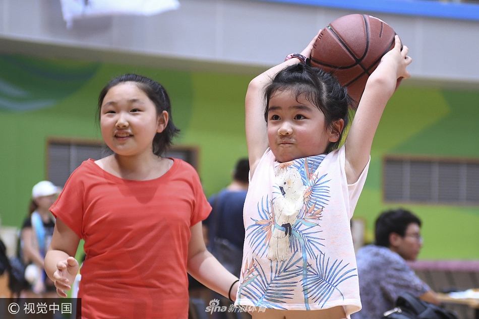 小沁蕾站在球场边，稚气未脱的脸上满是认真，她双手稳稳抱住一颗篮球，眼神专注，仿佛在思考如何像爸爸那样投出完美的一球。