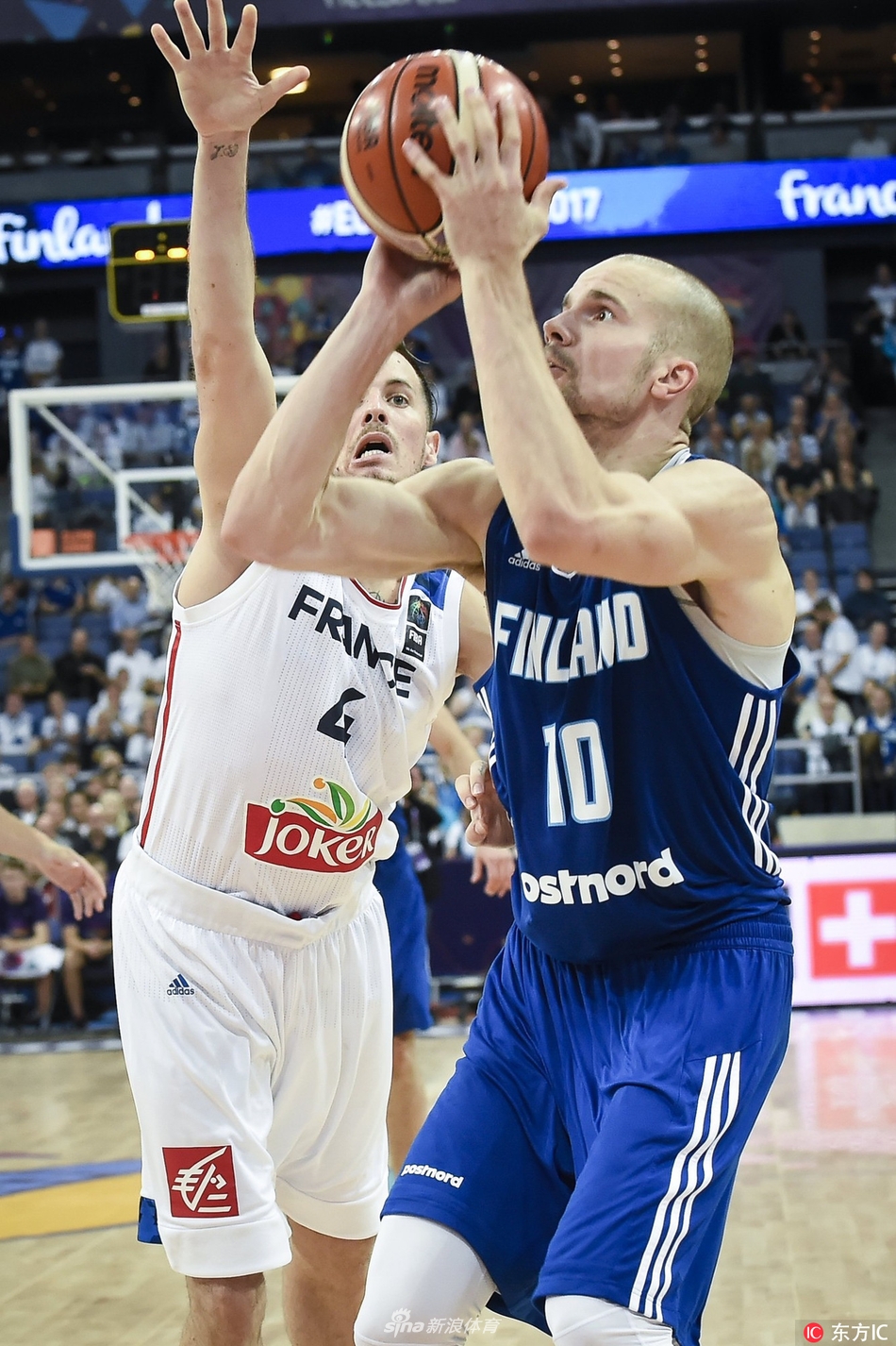 芬兰队7号新星马尔卡宁面对法国防守球员，高高跃起，眼神坚定地投出三分球的瞬间，全场球迷屏息凝视。