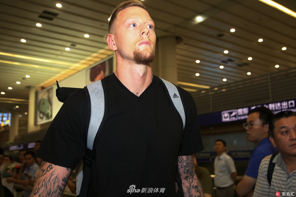 明纳拉斯与妻子在行李提取处等待，两人侧身相望，眼神交汇间传递着无需言语的默契，背景是繁忙的机场到达大厅