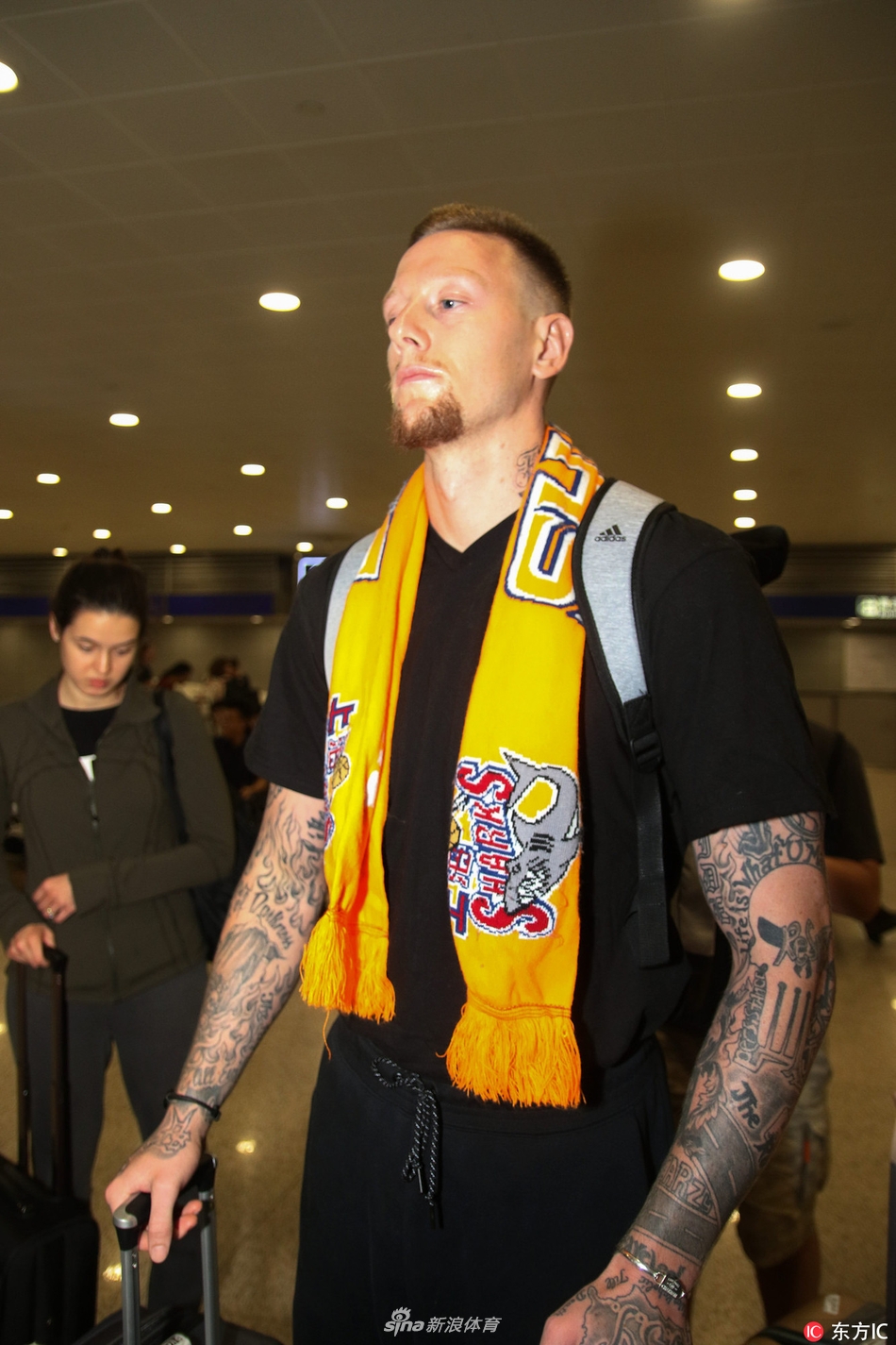 明纳拉斯在机场接受采访，他手持话筒神情专注而放松，身边的新婚妻子则以温柔的目光注视着他，画面充满了温馨与信任感