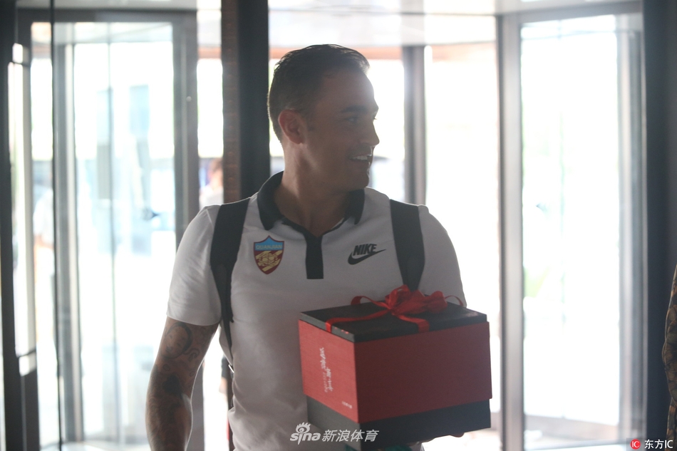 面带迷人微笑的卡纳瓦罗低头俯身,眼神中充满关切与温柔,耐心倾听一位日本女球迷的倾诉,后者手捧精心包装的礼物,脸上洋溢着见到偶像时的激动与羞涩,背景是天津略显萧瑟的初秋训练场,整个画面充满了温馨的追星色彩。