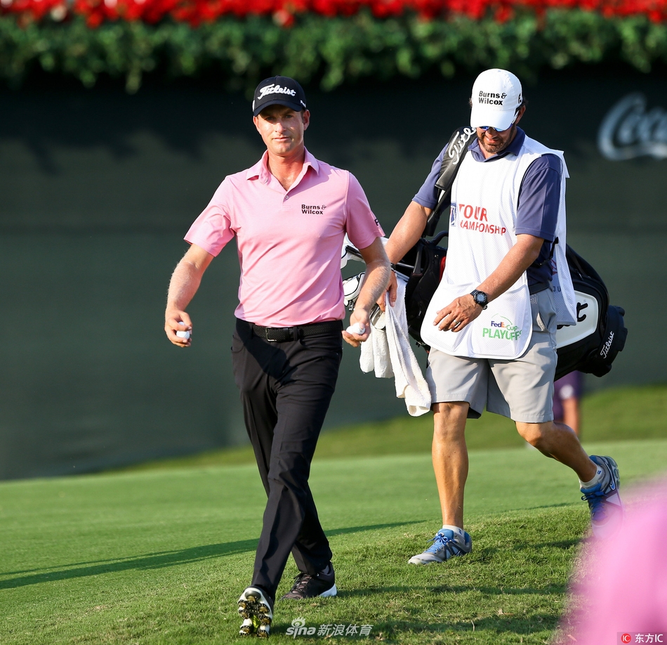 贾斯汀-托马斯在东湖球场第十八洞果岭旁，凝神审视推杆线路，远处记分牌映衬着他专注的身影