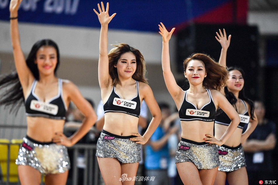 拉拉队员们围成一个小圈，中心一位队员做出高难度的空中劈叉动作，周围的队友们纷纷伸出双手给予保护，展现了团队之间的信任与默契