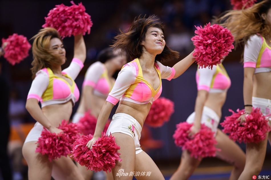 镜头聚焦于一位正在热舞的啦啦队员,她上身白色紧身衣勾勒出优美的线条,下身蓝色热裤格外亮眼。她面带自信的微笑,正随着音乐节奏摆动手臂,身后的队友们形成了整齐的队列。