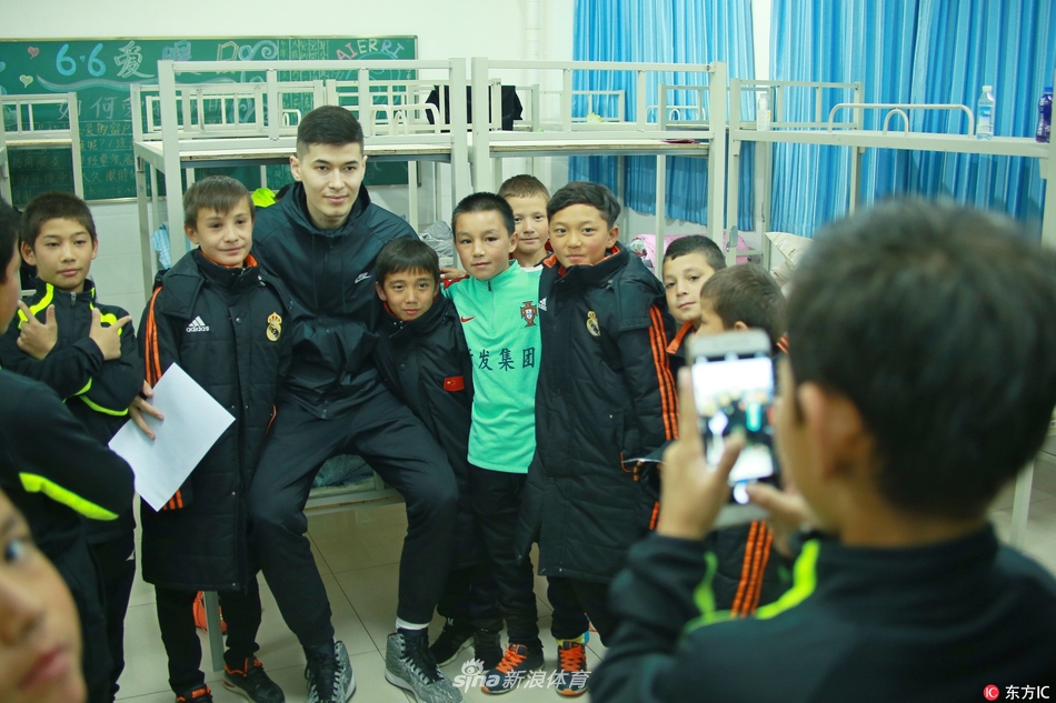 新疆男篮球星阿不都-沙拉木面带微笑,亲切地搂着几位穿着足球装备的小球员肩膀,眼神中满是鼓励与期许。