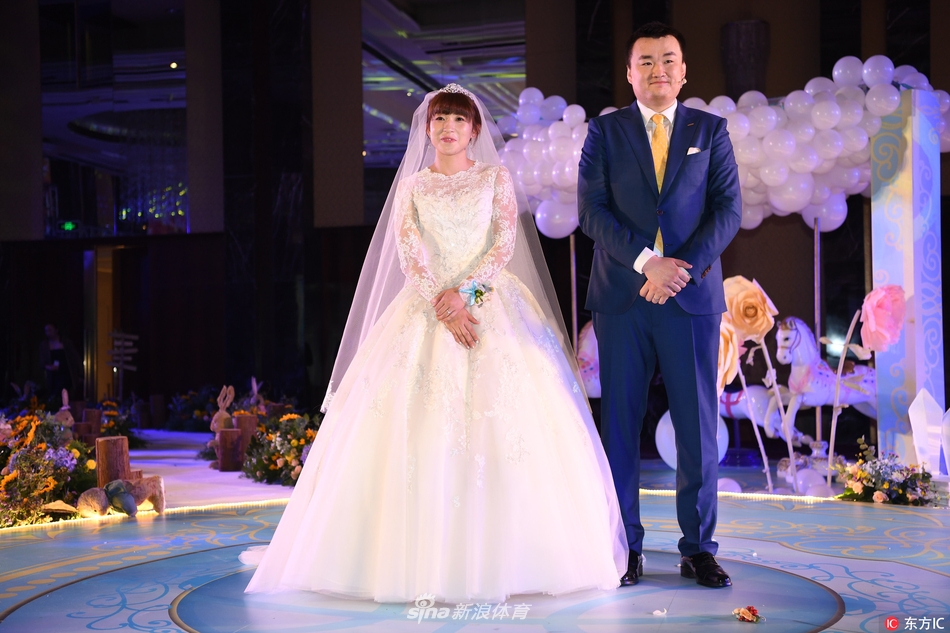 杨半伴与亲友们在婚礼上合影留念，她手举大红包，笑容灿烂，背景是喜庆的红色中式装饰。