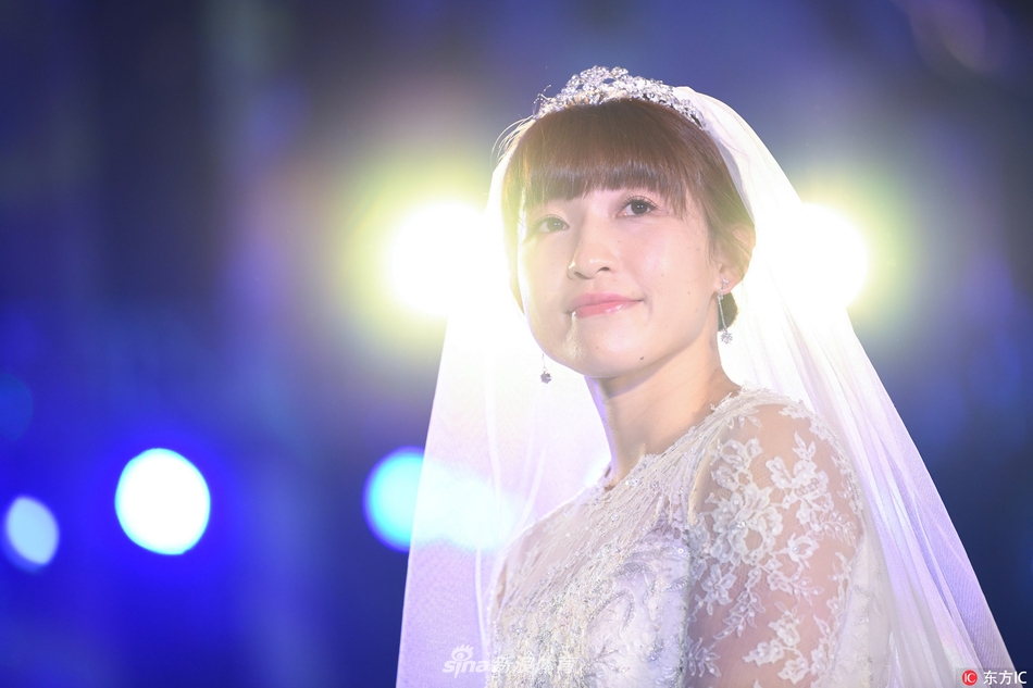 杨半伴与身穿灰色西装的丈夫甜蜜相依，新娘手捧红色玫瑰，新郎轻挽她的腰肢，画面充满了新婚的甜蜜与温馨。