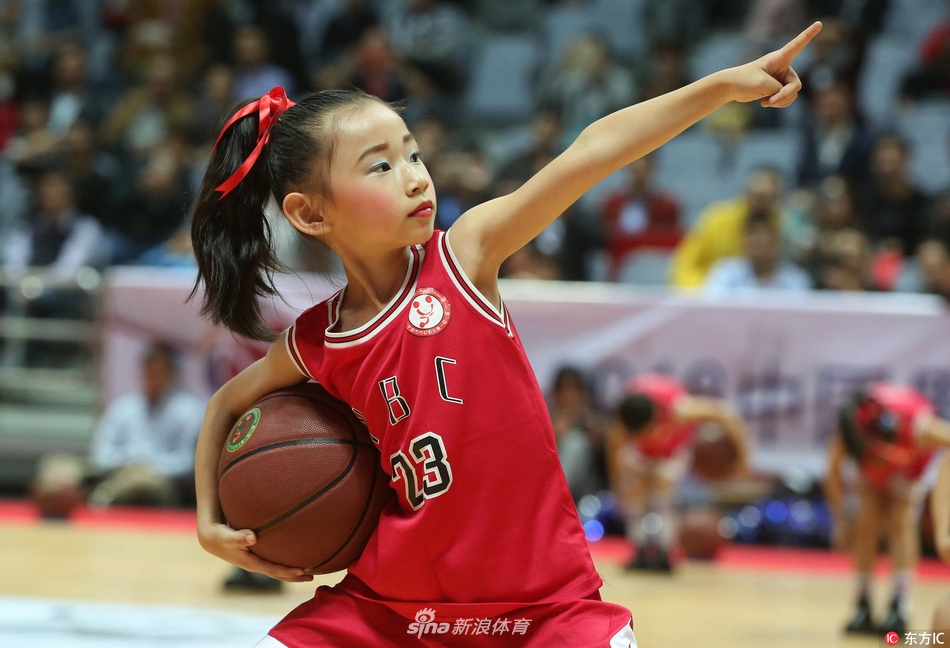 一个小球员紧紧抱着比自己小不了多少的篮球，安静地站在场边，望着远处正在热身的职业球员，眼神里充满了憧憬与向往。