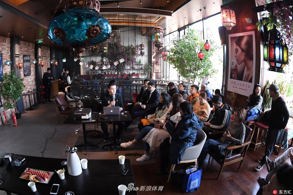 活动现场大屏幕上正在播放CBA比赛录像，画面定格在一次争议判罚的瞬间，两名裁判手持教鞭指向屏幕，向台下媒体进行讲解。