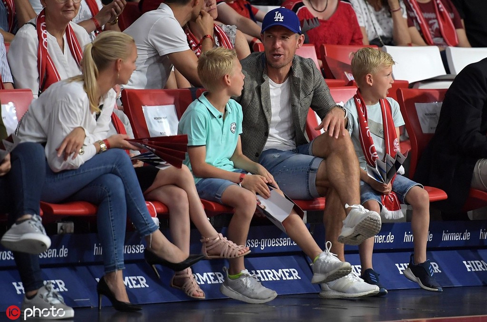 罗本的一个孩子兴奋地指向球场，罗本则弯腰倾听，画面充满了亲子互动的温情