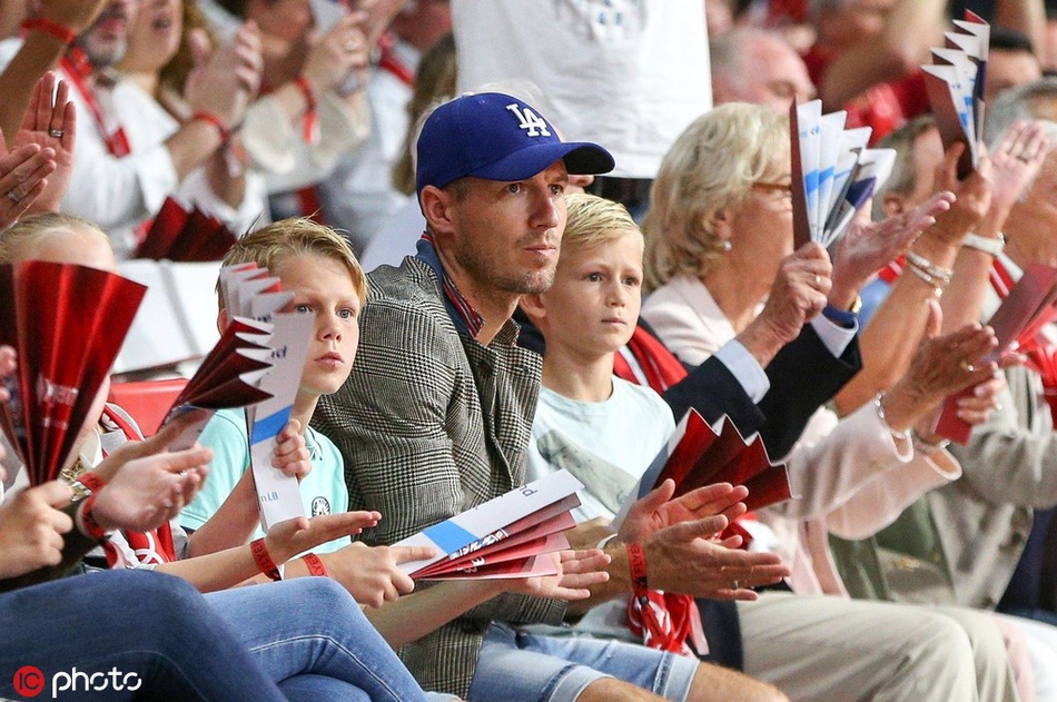 比赛间隙，罗本一家起身，罗本身穿深色T恤，面带笑容，准备离开座位