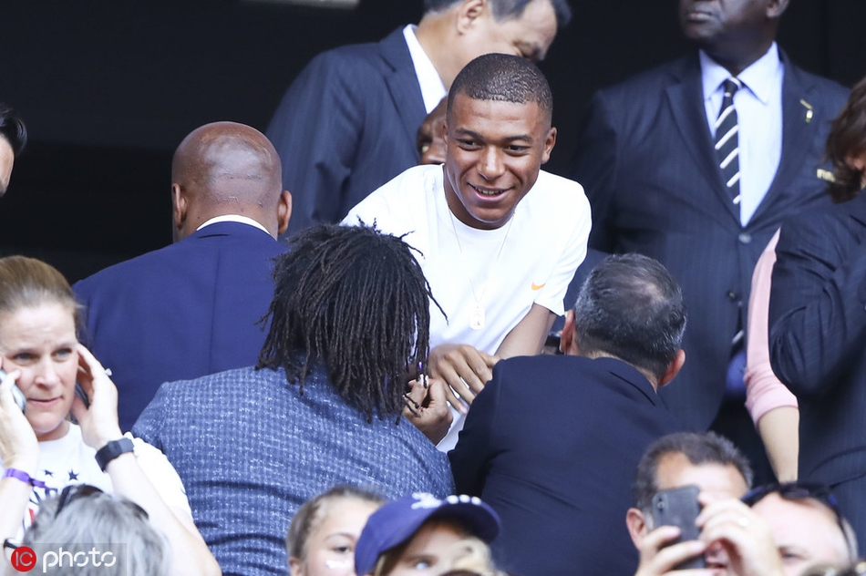 夺冠后美国女足队员相互拥抱庆祝，背景是欢呼的球迷看台。德罗巴等人也站起身来，为美国队的出色表现送上掌声，这一刻胜负与性别无关，只有对足球的敬意。