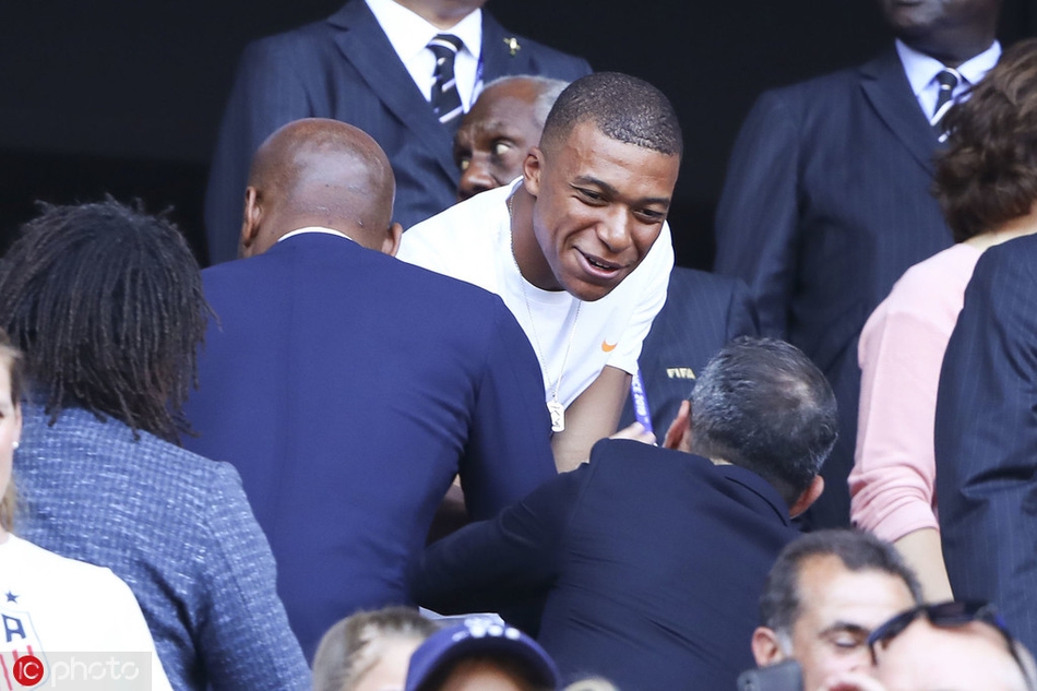 看台上的德罗巴与卡伦布神情严肃地交流着对比赛的看法，他们手指球场，似乎在分析美国与荷兰两队的战术布置，展现出专业球员的独特视角。