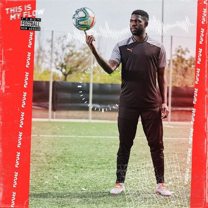 法国球星格列兹曼单手轻松托起新球，脸上洋溢着自信而调皮的笑容，背后的光线勾勒出他作为顶级射手的敏锐轮廓。