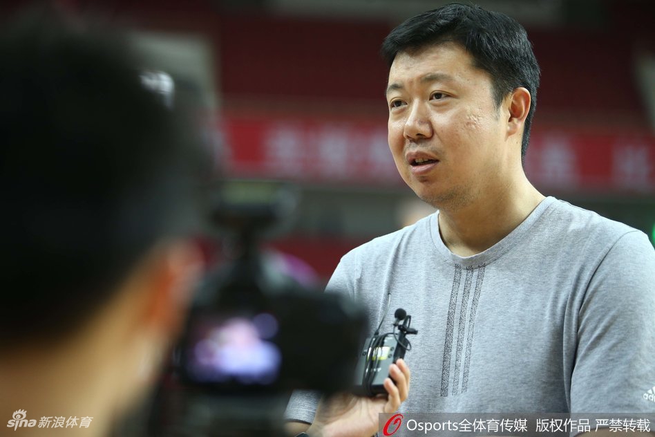男篮名宿王治郅在场边接受采访，目光深邃地注视着赛场动态，神情专注而严肃