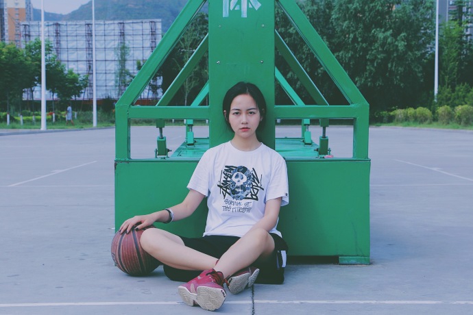 孙夕雨身穿休闲运动背心,头戴棒球帽,手拿篮球站在球场边,眼神清澈明亮,展现出邻家女孩的运动活力。