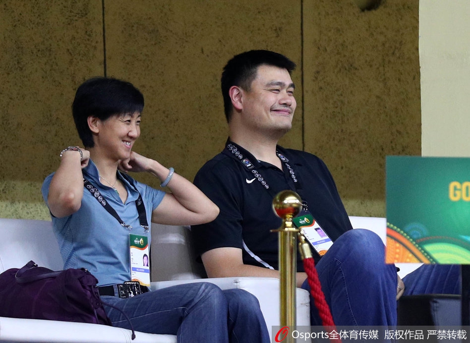 身着一袭淡蓝色衬衫的姚明端坐于看台，如山般沉稳的身形与周围观众形成鲜明对比，刚毅的面庞上，嘴角已不自觉微微上扬，仿佛对即将到来的比赛充满了期待。