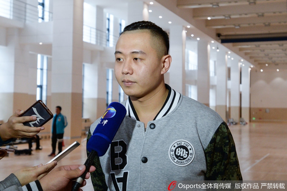 主教练徐贵军被球员们簇拥着看向镜头，他脸上挂着慈祥又略带腼腆的笑容，平日训练场上的严厉此刻化作了与弟子们同乐的温情，画面充满了人情味。