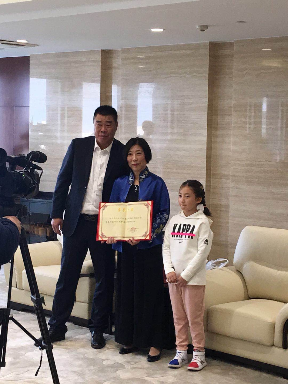 马布里弯腰俯身在捐赠支票上签名，张阿姨则在一旁满眼欣慰地注视着他的每一个动作，仿佛在欣赏自己孩子取得的成就。