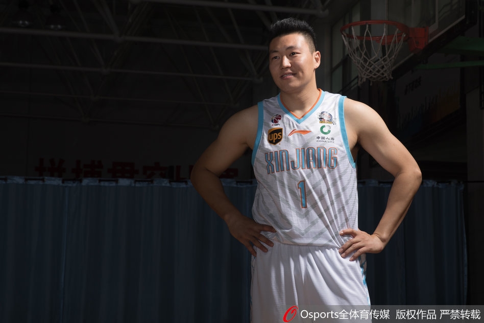 可兰白克-马坎身披新疆队战袍，双手叉腰站立，目光如炬凝视前方，队长袖标在灯光下熠熠生辉，仿佛在无声宣告着守护球队荣誉的誓言。