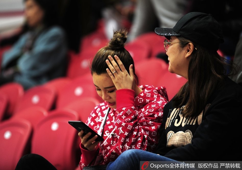 李根妻子王星洋扎着清爽丸子头,侧颜轮廓精致,身穿休闲外套坐在看台上,目光越过人群投向赛场方向,眼神中充满期待。