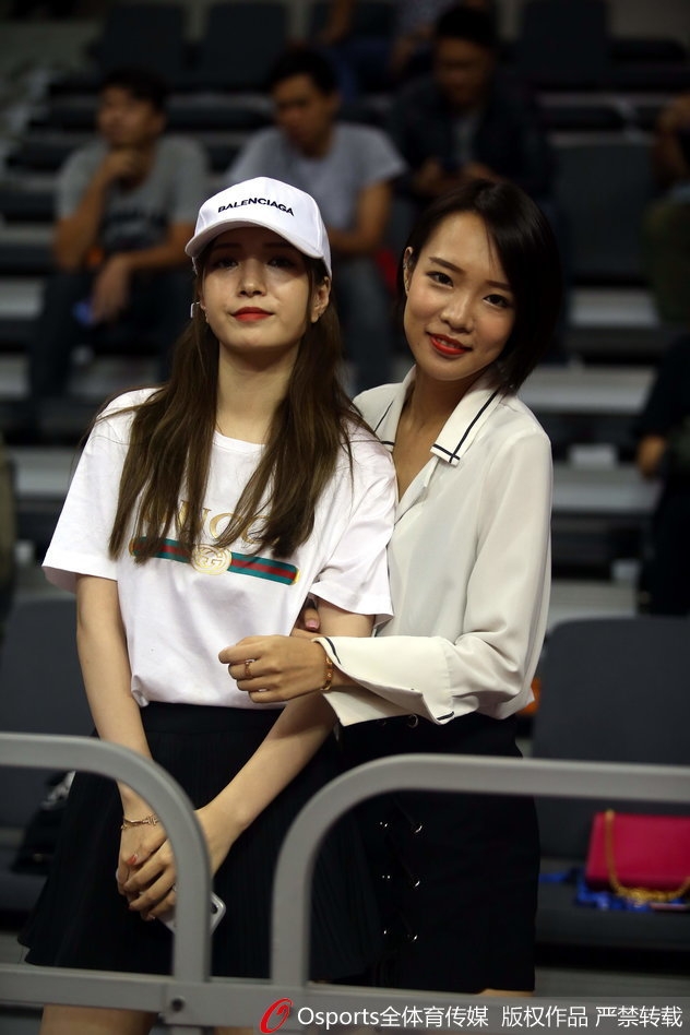 一位长发披肩的女球迷侧身望向场内,嘴角带着若有若无的笑意,精致的侧颜在球场灯光下格外引人注目。