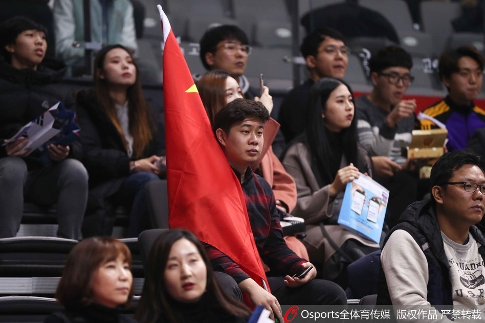 在韩国主场高阳体育馆的看台上,一名中国球迷神情专注且骄傲,双手奋力展开一面巨大的五星红旗,旗帜如火焰般在异国他乡的球馆内舒展。