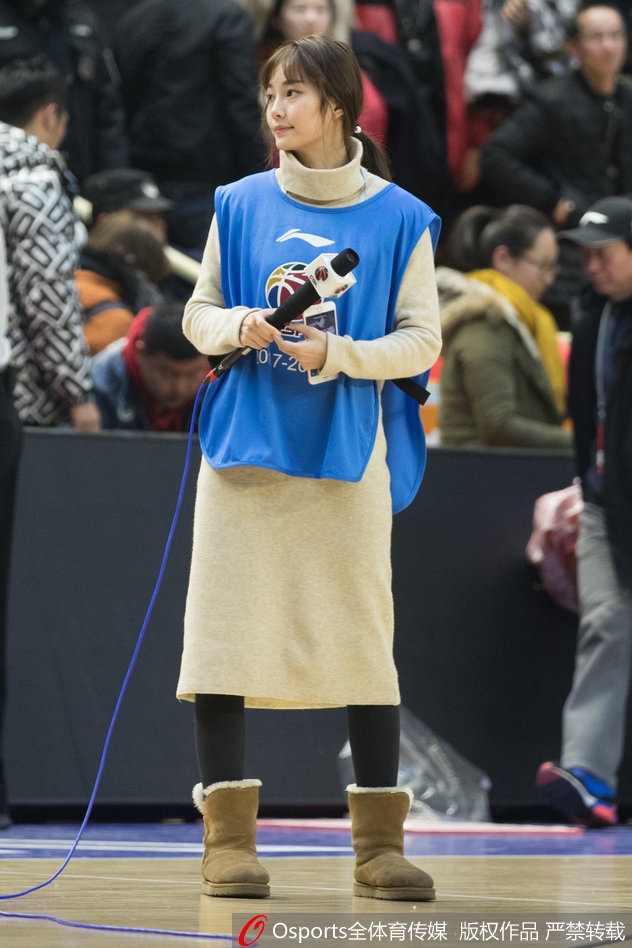 镜头拉近，美女主持轻倚场边广告板，一头秀发自然垂落，眼神清澈而坚定，仿佛正用无声的语言为广厦队加油打气。