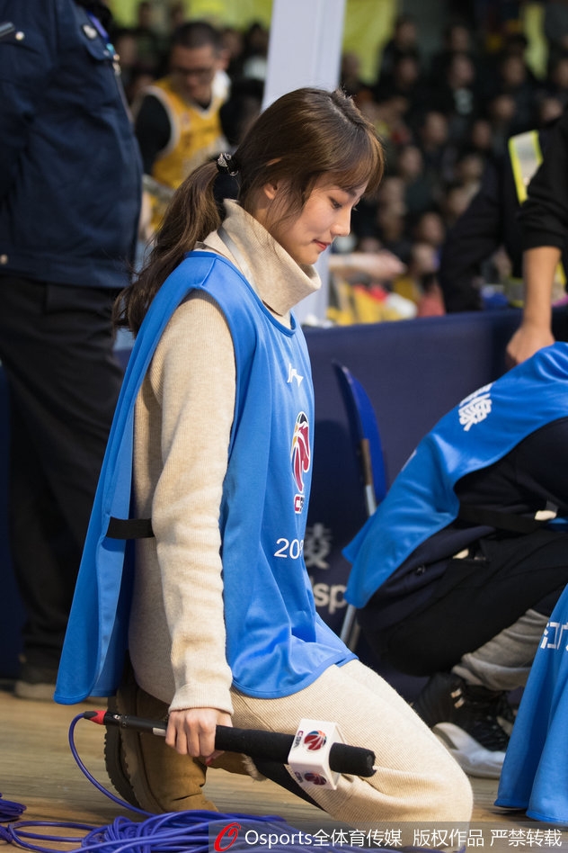 工作间隙，美女主持手拿纸质资料，倚靠在通道墙边，简单随性的姿势难掩其温婉气质，仿佛在思考下一节如何调动现场气氛。