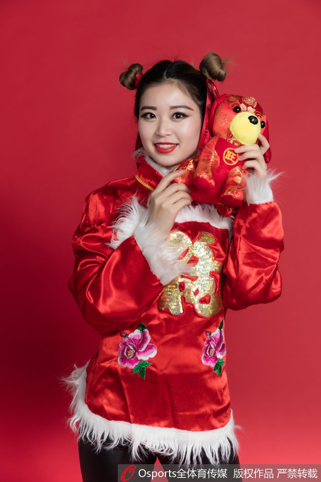 宝贝轻抚发髻，一身明艳民俗装束在红色背景衬托下更显喜庆，眉眼间流露的娇俏与温柔，恰似新春最美好的祝福。