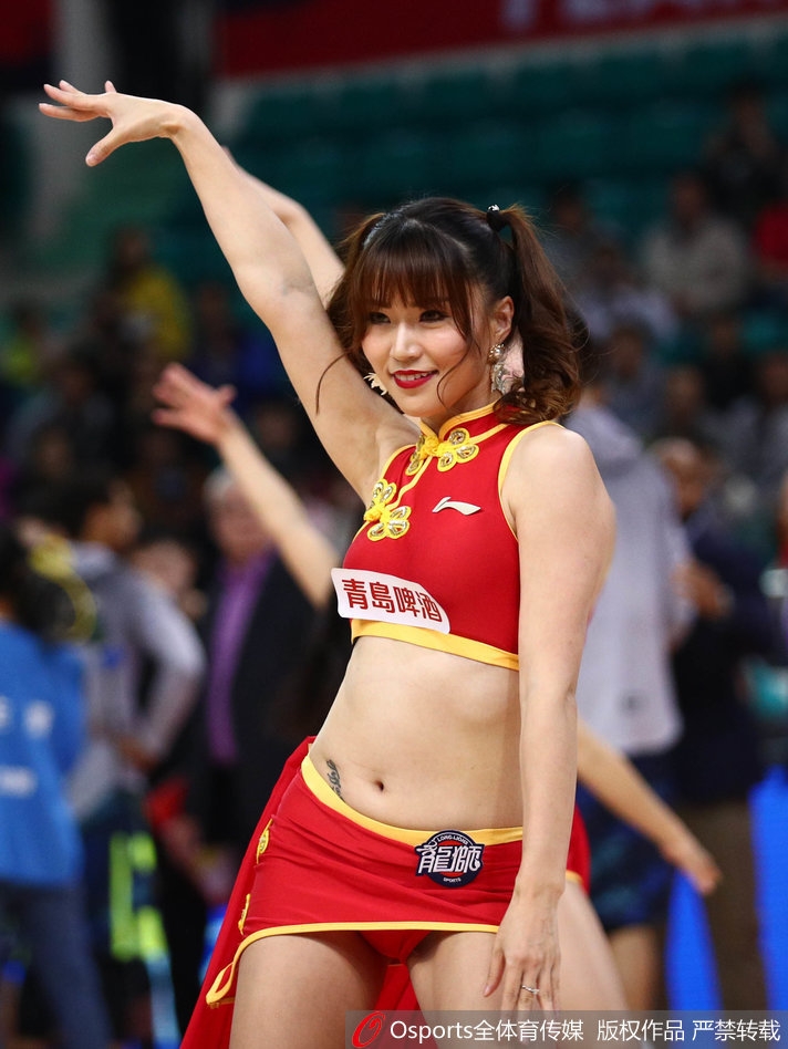 镜头拉近，这位篮球宝贝脸颊上贴着亮片，她轻抿嘴唇，眼神中透露出专注与灵动，身后的队友身影虚化，更凸显了她此刻的迷人神态。