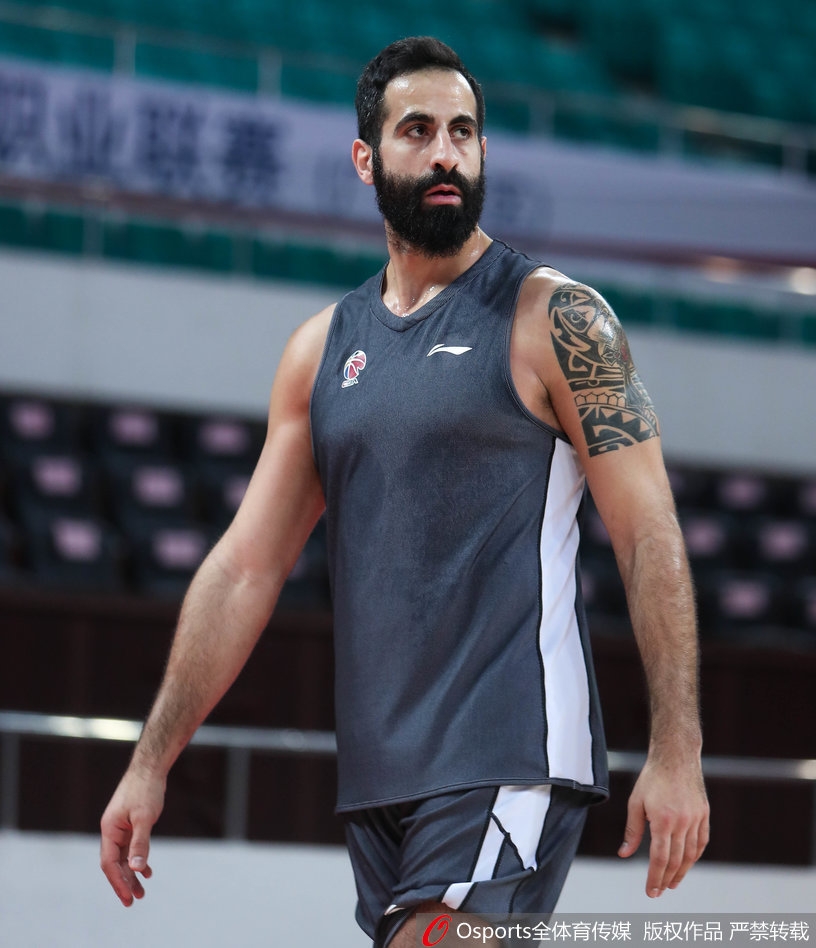 广州队球员在助教的协助下进行赛前拉伸，球员表情专注，身体线条舒展，身后的队标清晰可见，备战氛围专业而有序。