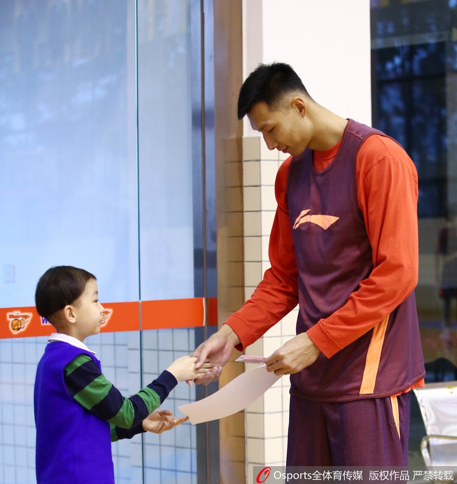 轩轩手持签名篮球,与身穿训练服的广东宏远队员面对面交流,队员俯身倾听轩轩说话,画面温馨感人。