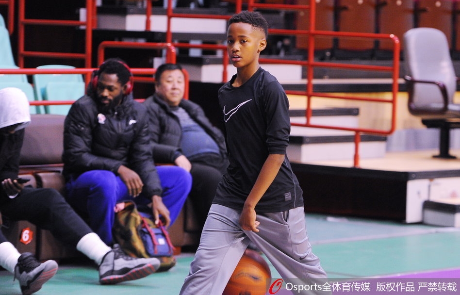 巴斯儿子双手举着篮球准备投篮,动作有模有样,巴斯在场边微笑观看