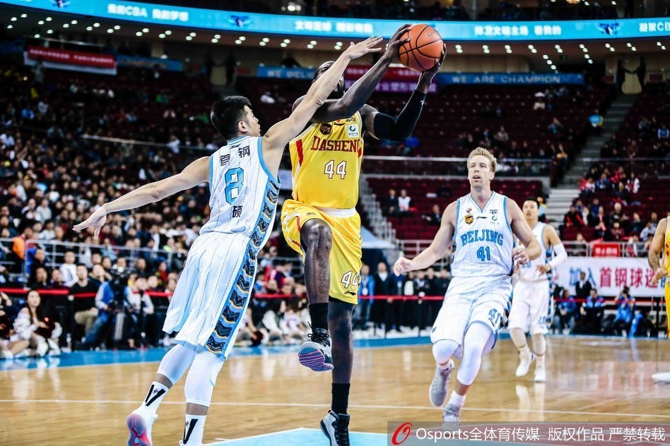 赛后，北京首钢球员们围成一圈，互相击掌鼓励，脸上洋溢着胜利的喜悦，背景是五棵松体育馆内飘扬的旗帜。