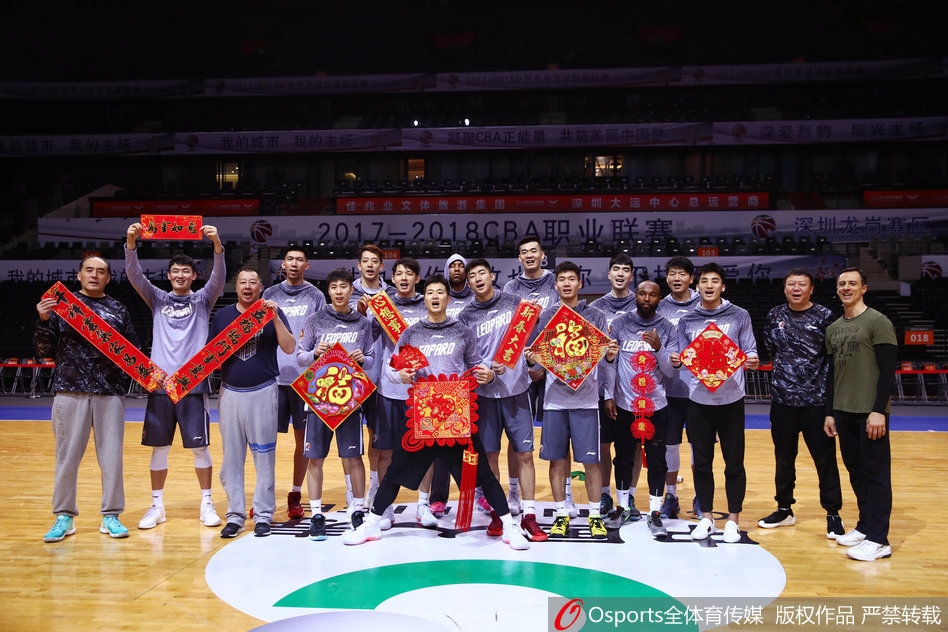 主教练王建军指导在拍摄现场露出难得的轻松微笑，他与外援萨林杰并肩而立，两人手中拿着春联，仿佛在战术板上画出了一幅新春取胜的蓝图。