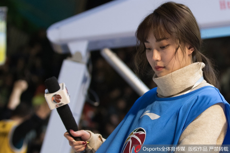 在明亮的场馆灯光下，美女主持侧身回眸，嘴角带着浅浅笑意，那份从容与优雅与身后座无虚席的看台相映成趣。