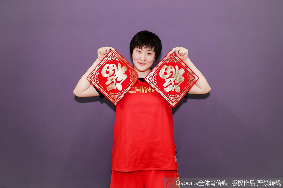 全体队员与教练组的大合影，大家簇拥在一起，有的竖起大拇指，有的挥舞着国旗，画面中充满了积极向上的能量，完美诠释了中国女篮团结拼搏的精神风貌。