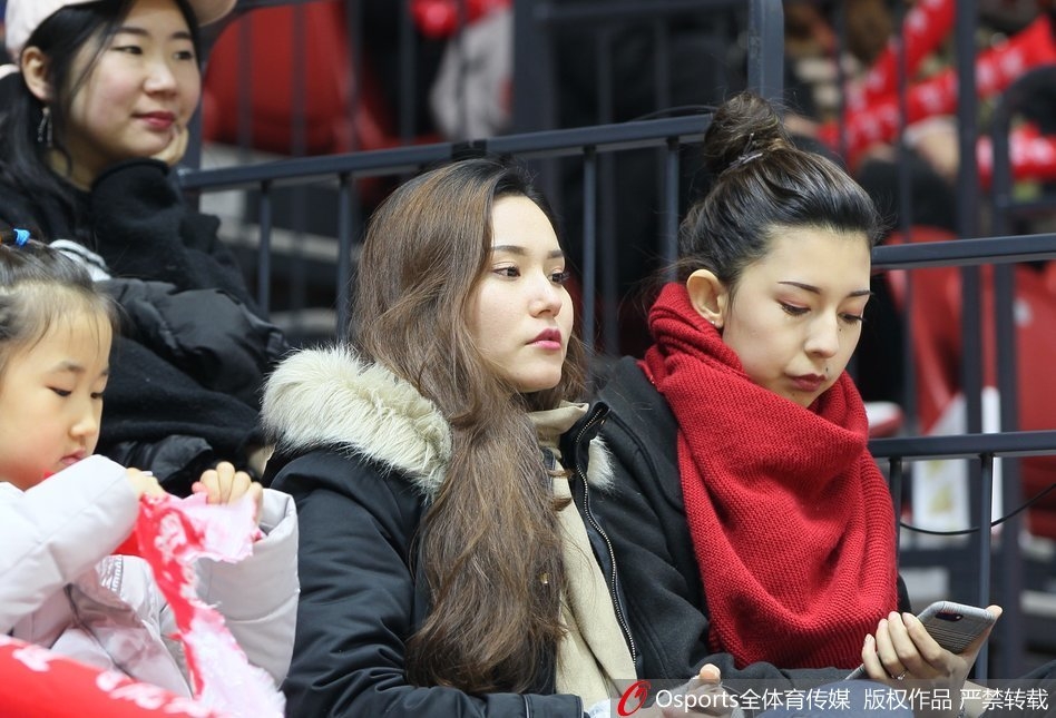 一头利落短发的女生用手轻触帽檐，眼神清澈而坚定。她以一种酷酷的姿态融入球馆的背景，既像是观察者，又像是这场篮球盛宴的时尚主角。