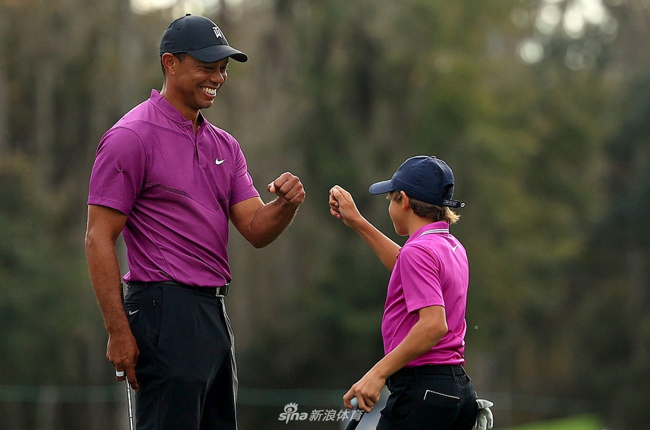老虎伍兹与儿子查理在开球前专注商讨策略，阳光洒在绿茵场上，父子二人的身影构成一幅温馨而专业的画面。