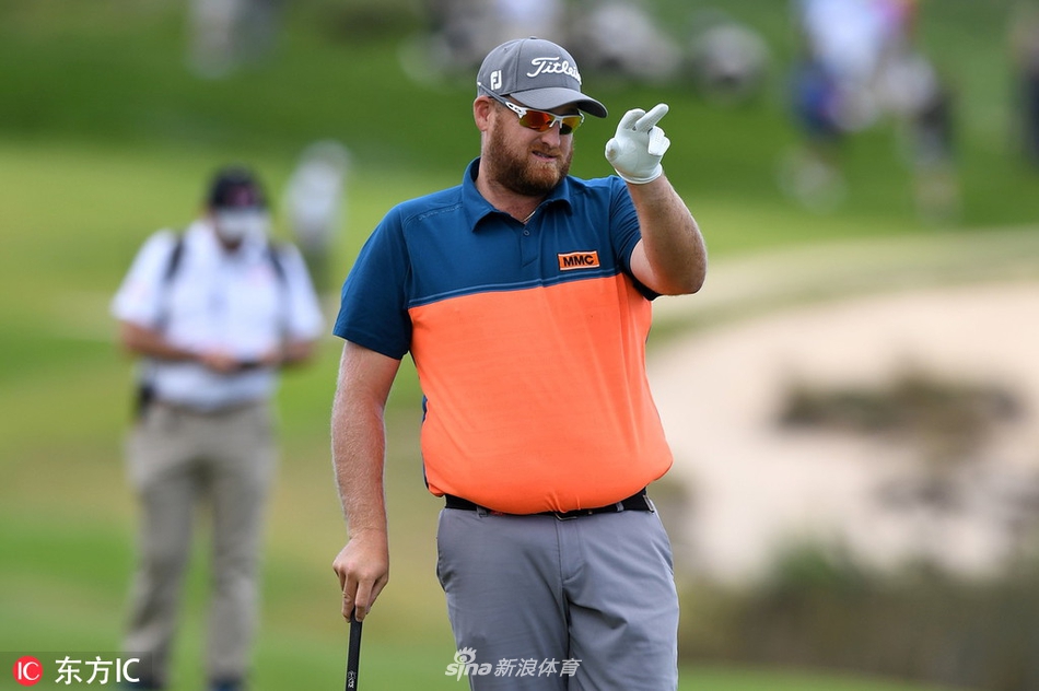 安瑟在第十八洞球道上凝神思考第二击策略，阳光拉长了他的身影，远处观众席座无虚席。