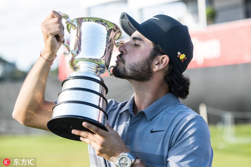 安瑟在沙坑中全神贯注地准备一击，沙粒在阳光下闪烁，背景是蔚蓝天空与起伏的果岭。