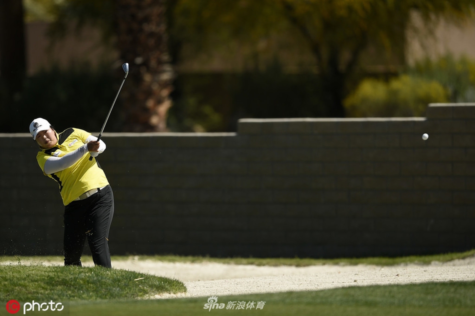球员在沙坑中救球，沙粒飞扬，展现高尔夫运动技巧与力量的瞬间
